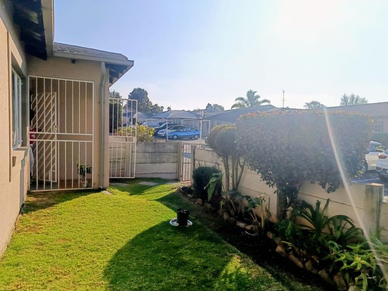A private rear garden area featuring a lawn, established garden beds, and a secure gated entrance to the townhouse property.