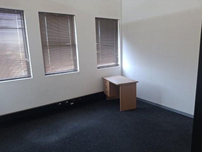 A vacant office space featuring neutral walls, dark carpeting, and multiple windows fitted with venetian blinds.