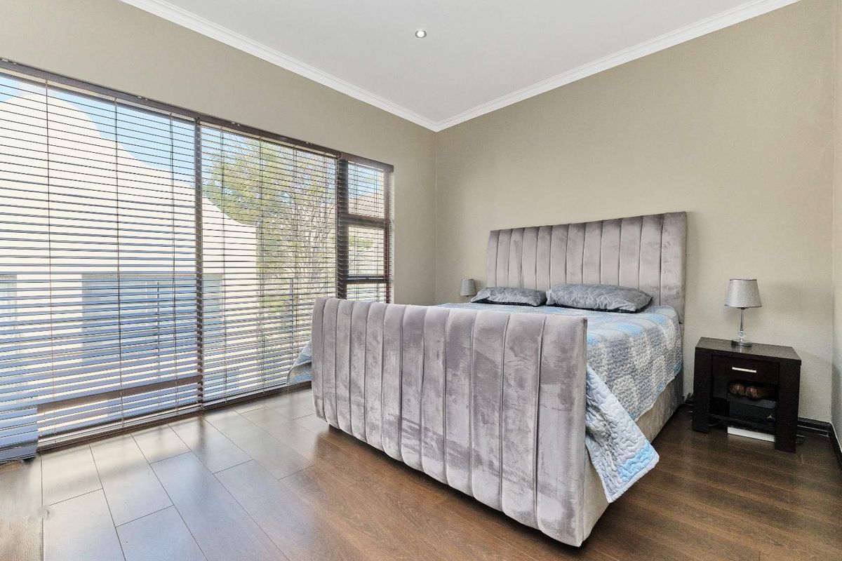 A well-maintained bedroom featuring dark wood-look flooring, neutral wall tones, recessed ceiling lighting, and large windows fitted with horizontal blinds.