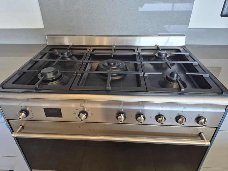 A modern stainless steel gas hob and built-in oven set into a stone countertop with a matching stone splashback.