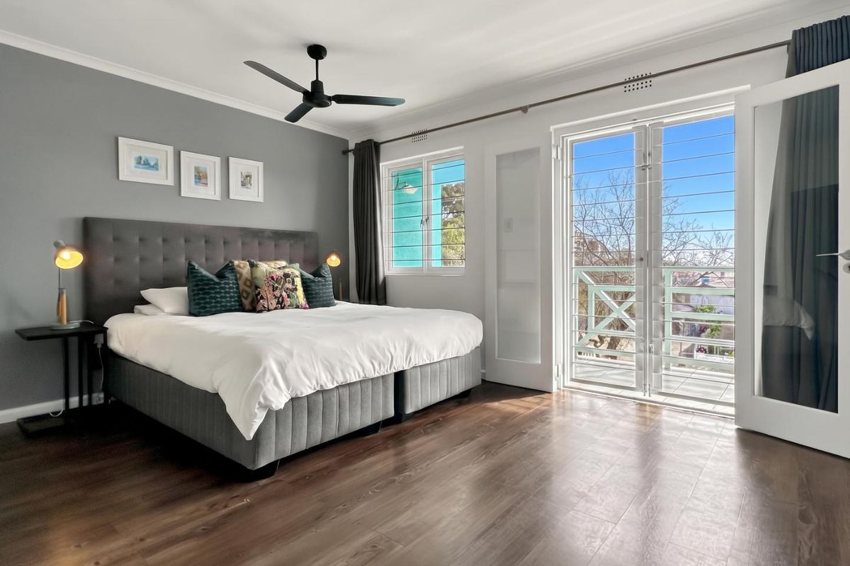 Spacious bedroom featuring dark laminate flooring, a ceiling fan, and direct access to a private balcony through glass-paned french doors.