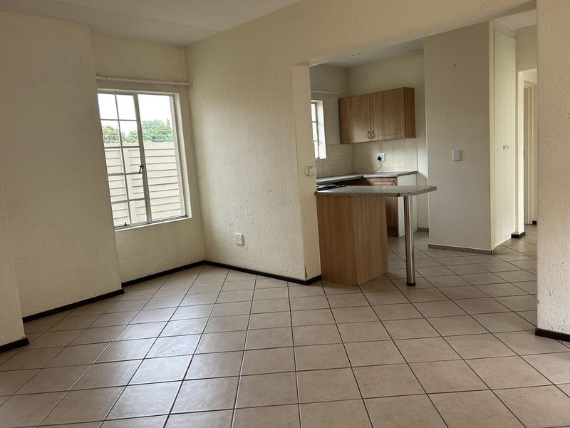 An open-plan living and kitchen area featuring tiled flooring, built-in kitchen cabinetry, and a breakfast bar, offering a functional and versatile living space.