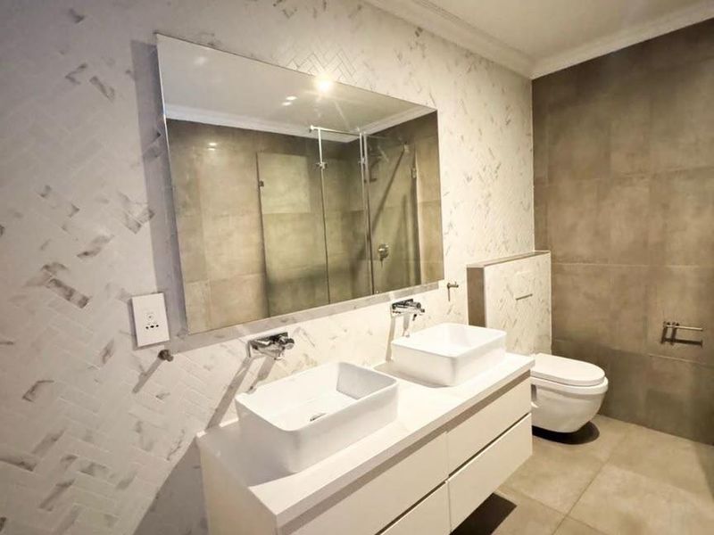 Modern bathroom featuring a floating double vanity with vessel sinks, wall-mounted faucets, a wall-hung toilet, and a glass-enclosed shower with contemporary tiling.