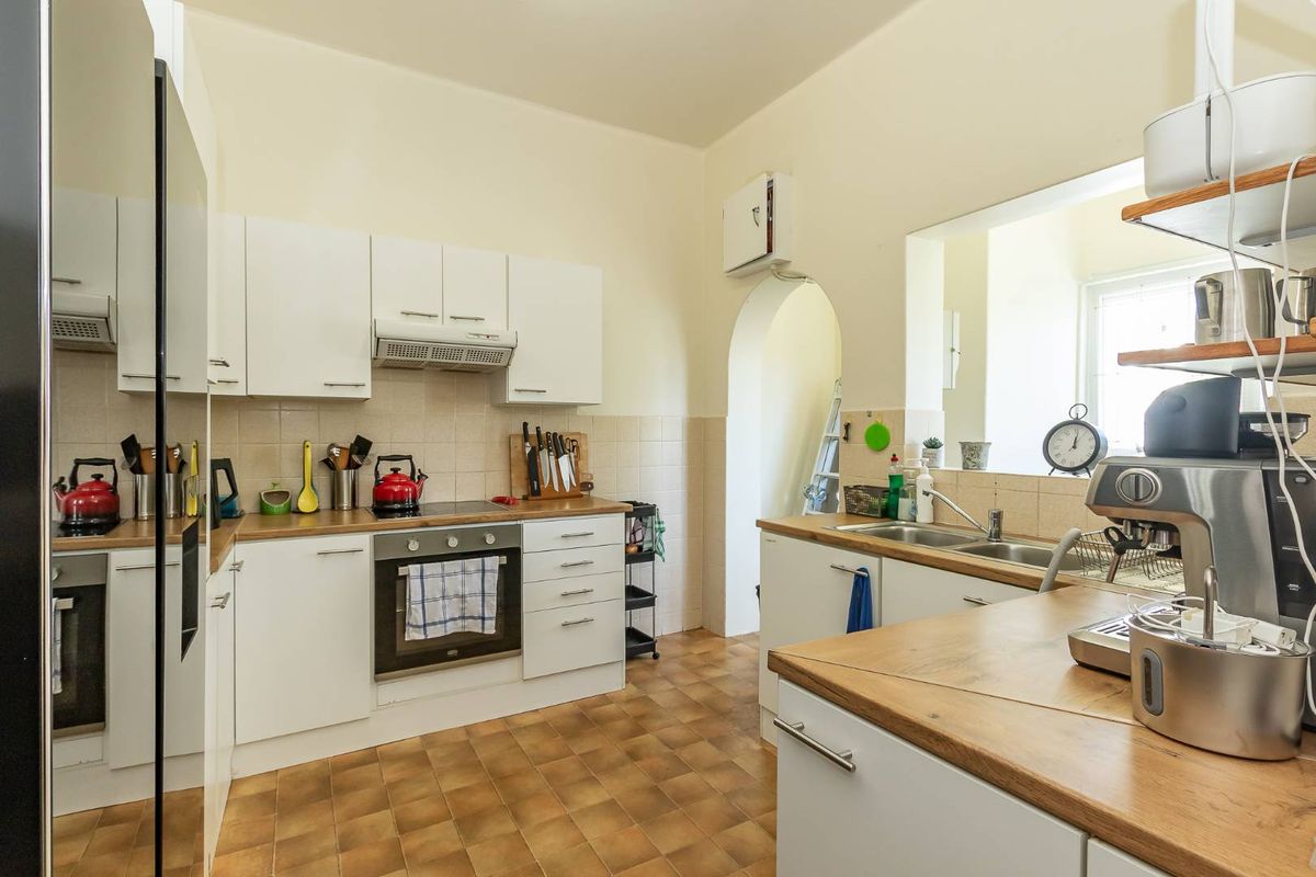 Functional kitchen featuring white cabinetry, wood-look countertops, built-in oven, extractor fan, and a double stainless steel sink with a serving hatch.