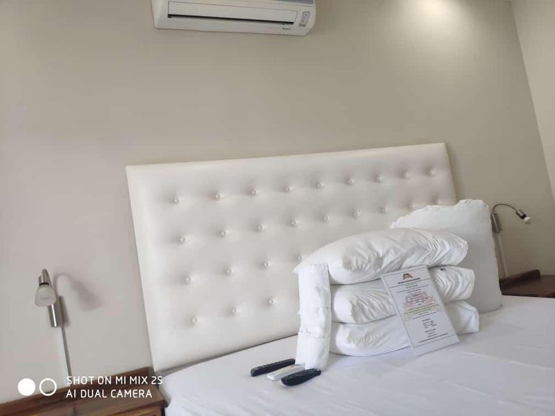 A bedroom featuring a tufted headboard, wall-mounted reading lights, and an air conditioning unit.