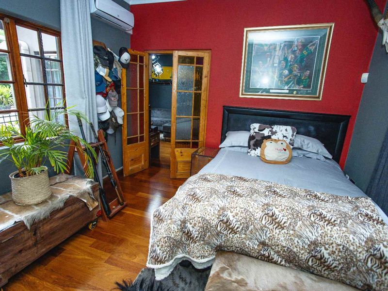 A bedroom featuring hardwood flooring, a wall-mounted air conditioning unit, and timber-framed french doors leading to an adjacent space.