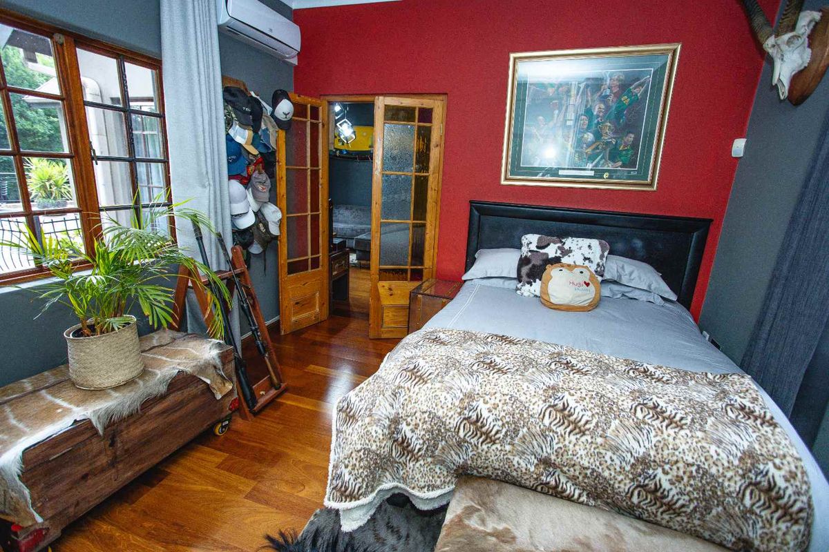 A bedroom featuring hardwood flooring, a wall-mounted air conditioning unit, and timber-framed french doors leading to an adjacent space.