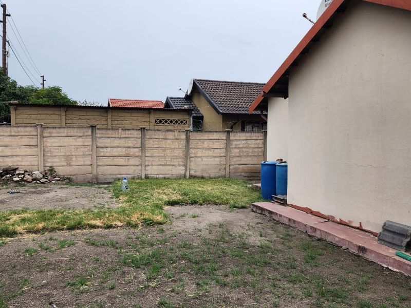 Rear exterior view of the property featuring a concrete boundary wall, a small lawn area, and the side elevation of the main dwelling.