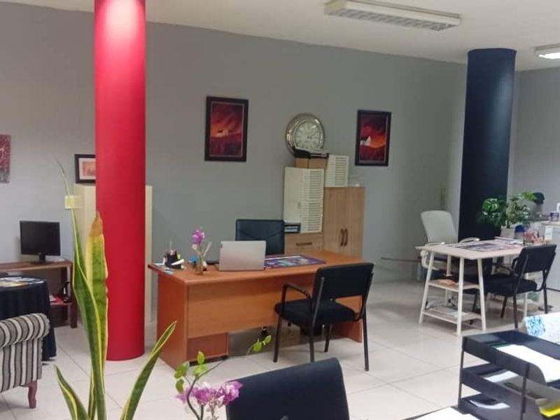 Open-plan office space featuring tiled flooring, structural columns, and overhead fluorescent lighting, providing a functional workspace environment.
