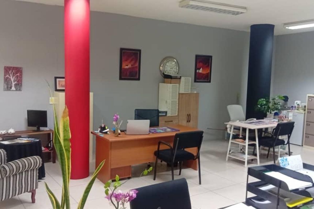 Open-plan office space featuring tiled flooring, structural columns, and overhead fluorescent lighting, providing a functional workspace environment.