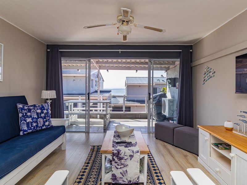 A bright living room featuring laminate flooring, a ceiling fan, and large sliding glass doors that open onto a balcony with coastal views.
