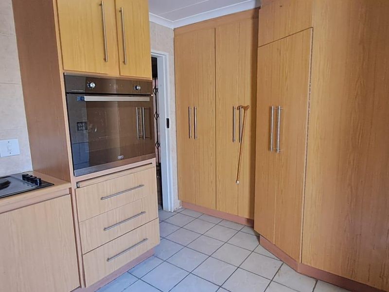 A functional kitchen featuring light wood-toned cabinetry, a built-in oven, electric hob, and tiled flooring with neutral wall tiles.