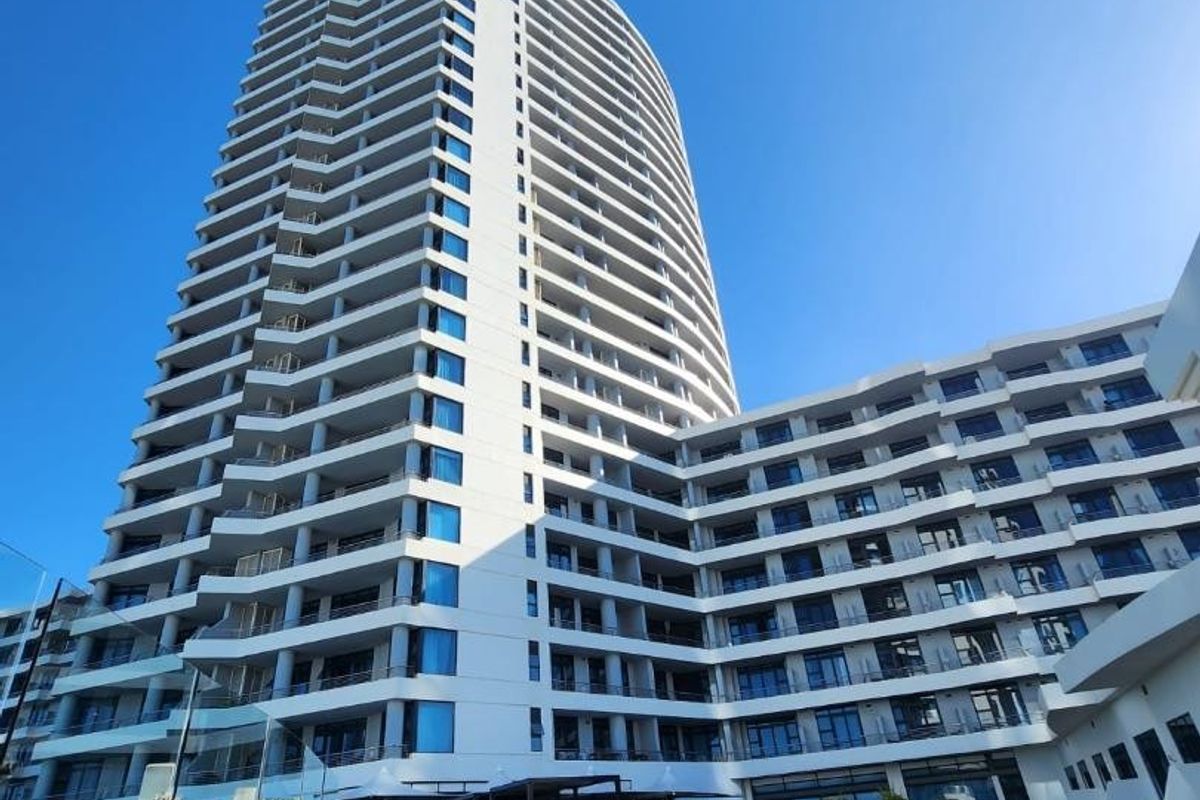 A low-angle view of a modern high-rise apartment building featuring extensive glass balconies and a landscaped outdoor terrace area.