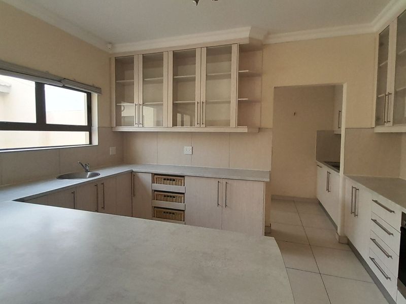 A clean, functional kitchen featuring light-toned cabinetry, stone countertops, integrated appliances, and a separate scullery area with tiled flooring throughout.