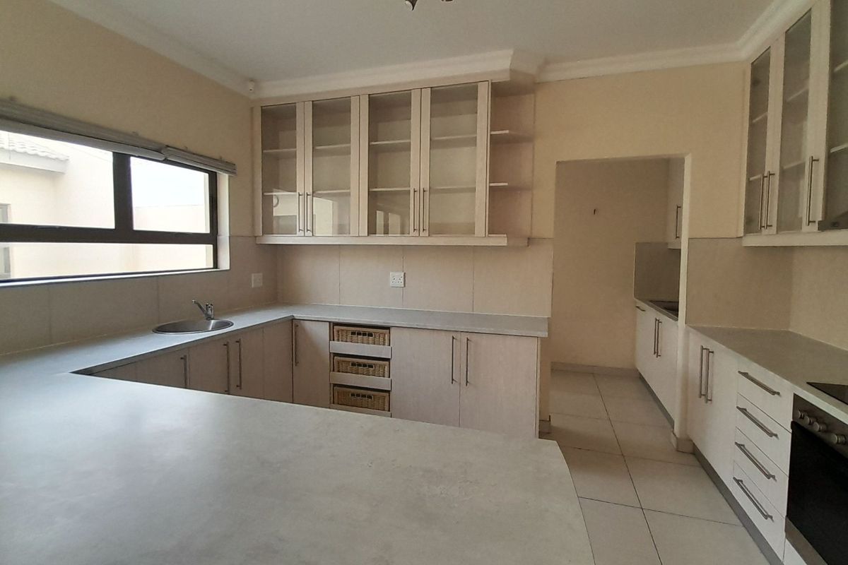 A clean, functional kitchen featuring light-toned cabinetry, stone countertops, integrated appliances, and a separate scullery area with tiled flooring throughout.