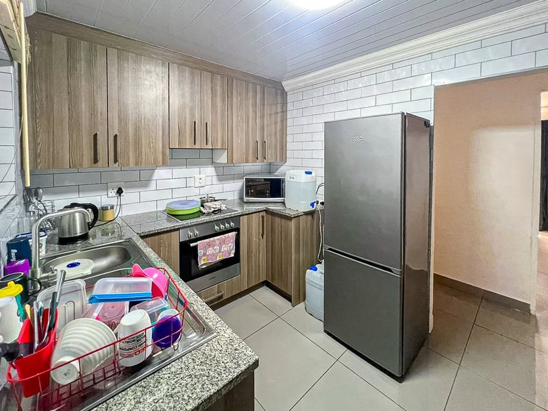 A functional kitchen featuring wood-look cabinetry, granite countertops, subway tile backsplash, and built-in oven, finished with tiled flooring and a panelled ceiling.