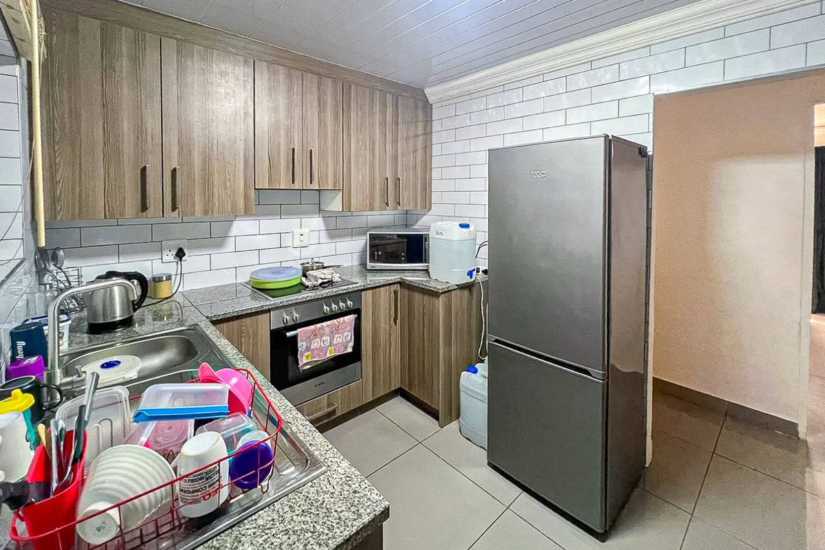 A functional kitchen featuring wood-look cabinetry, granite countertops, subway tile backsplash, and built-in oven, finished with tiled flooring and a panelled ceiling.