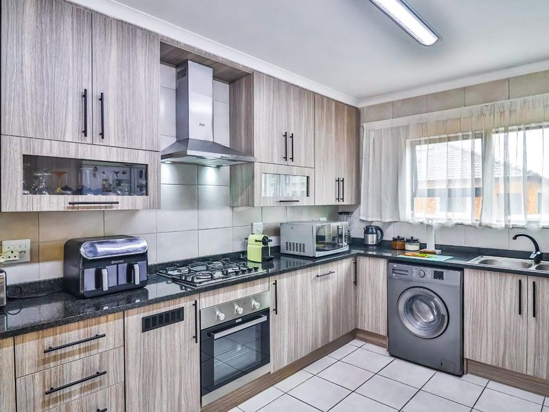 Modern kitchen featuring wood-grain cabinetry, granite countertops, a gas hob, built-in oven, extractor fan, and integrated space for a washing machine.