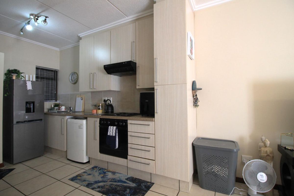 A functional kitchen featuring light-toned built-in cabinetry, laminate countertops, a built-in oven with hob, extractor fan, and tiled flooring.