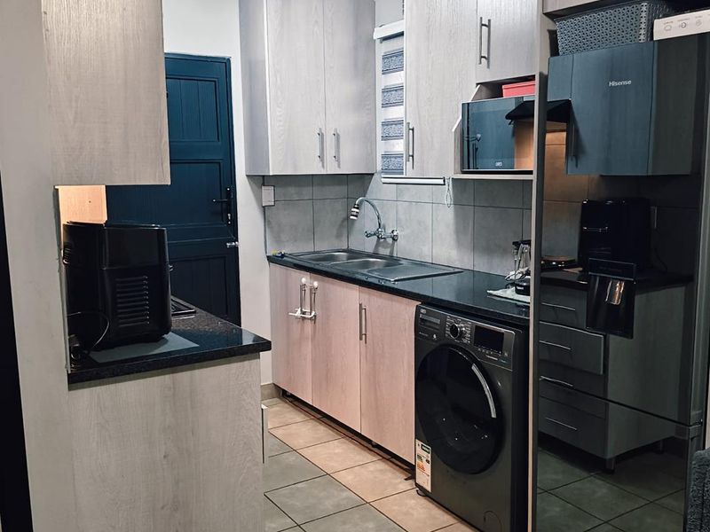 A functional kitchen featuring light wood-finish cabinetry, dark countertops, tiled flooring, and an integrated washing machine, providing a compact and efficient workspace.