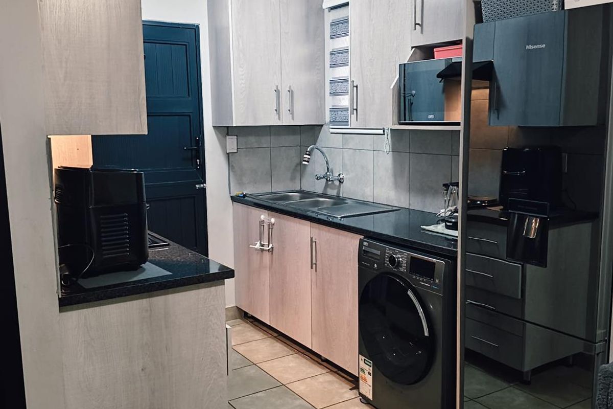 A functional kitchen featuring light wood-finish cabinetry, dark countertops, tiled flooring, and an integrated washing machine, providing a compact and efficient workspace.