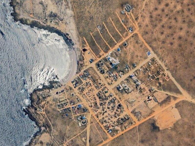 Aerial view of a coastal residential development area featuring unpaved roads and proximity to the ocean.