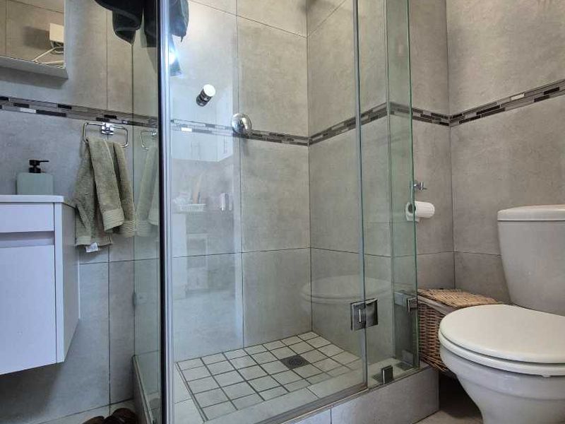 A modern bathroom featuring a glass-enclosed shower, wall-mounted vanity, and neutral grey floor-to-ceiling tiling.