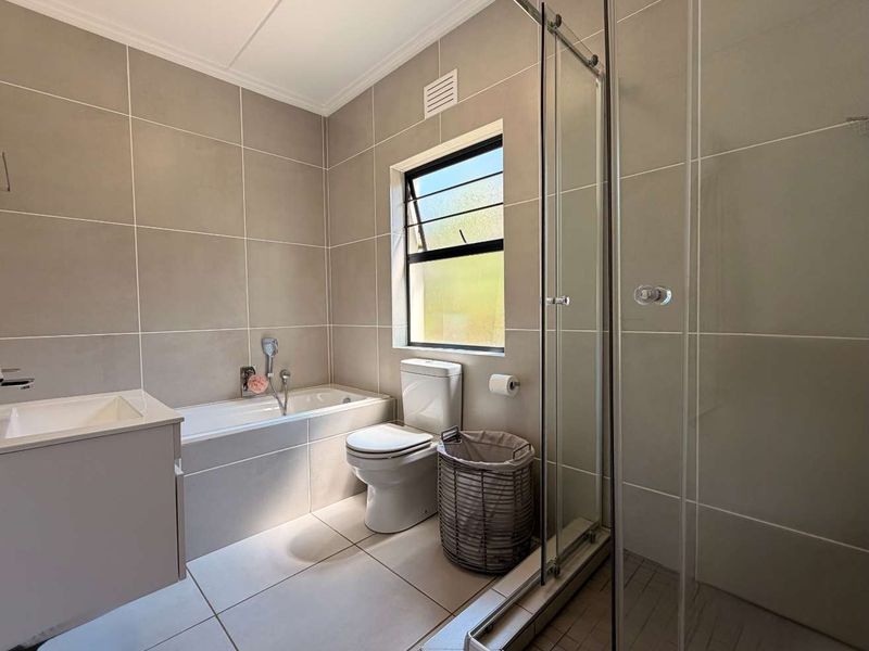A modern, well-maintained bathroom featuring neutral floor-to-ceiling tiling, a built-in vanity, a bathtub, and a separate glass-enclosed shower.
