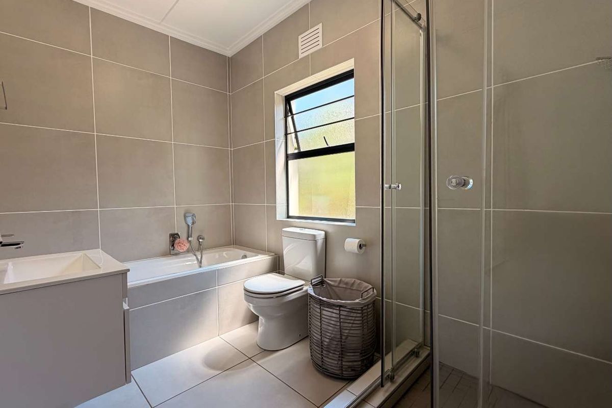 A modern, well-maintained bathroom featuring neutral floor-to-ceiling tiling, a built-in vanity, a bathtub, and a separate glass-enclosed shower.