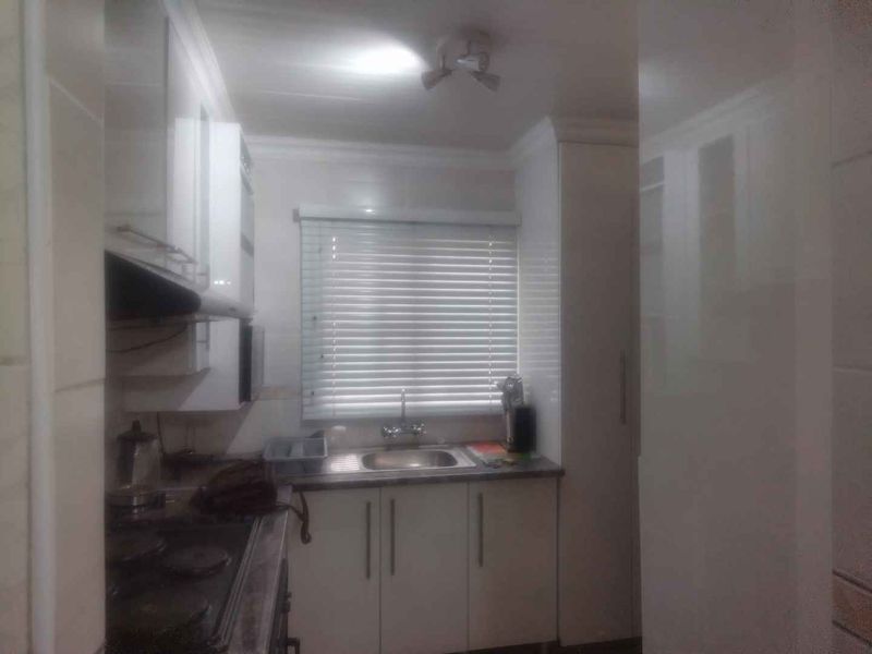 A compact kitchen featuring white built-in cabinetry, a stainless steel sink, and a fitted hob with an extractor fan.