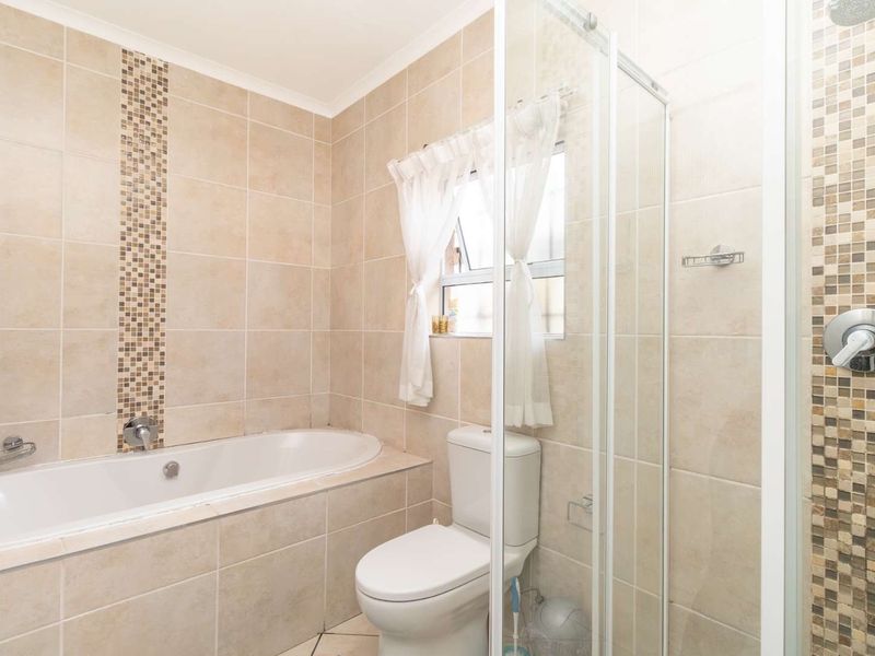 A well-maintained bathroom featuring a built-in bathtub, separate shower enclosure, and neutral tiled finishes with decorative mosaic accents.