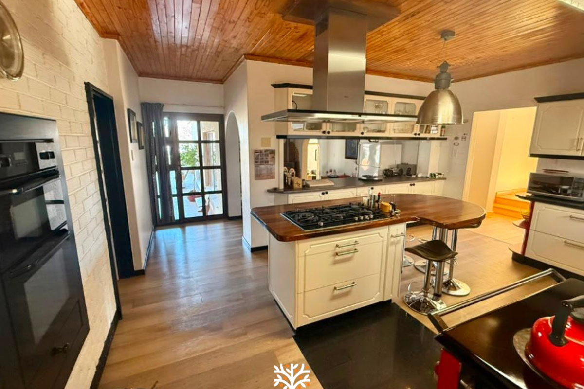 Spacious kitchen featuring a central island with a gas hob, timber ceiling, and built-in oven, offering a blend of rustic and modern finishes.