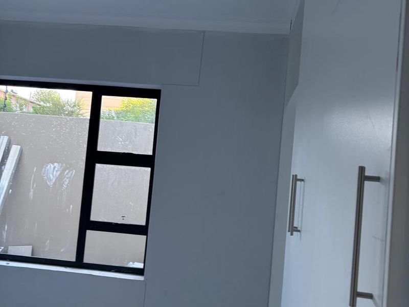 A vacant bedroom featuring tiled flooring, built-in cupboards, and an aluminium window frame, currently requiring final wall finishing and painting.