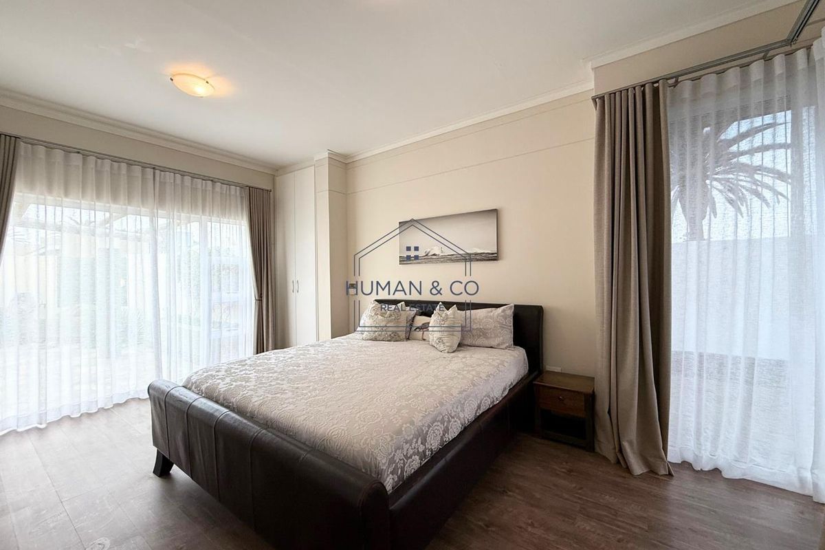 A well-maintained bedroom featuring built-in wardrobes, wood-look flooring, and large sliding glass doors providing access to the outdoor area.