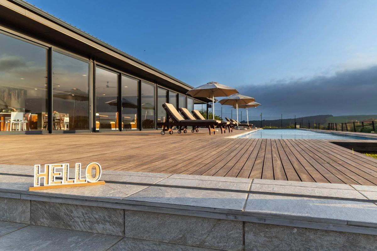 Spacious outdoor pool area featuring extensive timber decking, modern stone coping, and large sliding glass doors providing seamless indoor-outdoor flow.