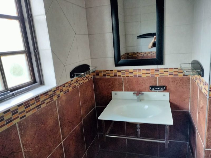 A functional bathroom featuring a wall-mounted basin with chrome mixer tap, complemented by decorative tiled walls and flooring.