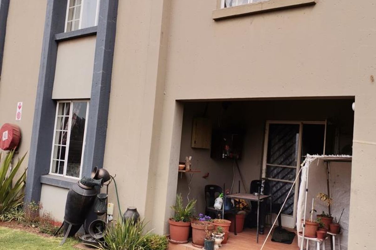 A view of the apartment's rear exterior, featuring a covered patio area, tiled flooring, and access to the garden space.