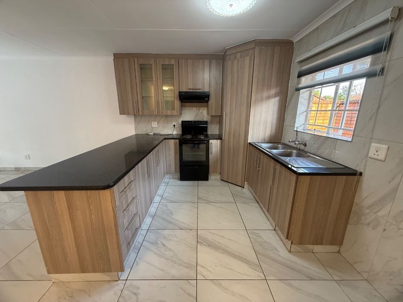 Modern kitchen featuring wood-finish cabinetry, granite countertops, a double sink, and a freestanding stove with an extractor fan.