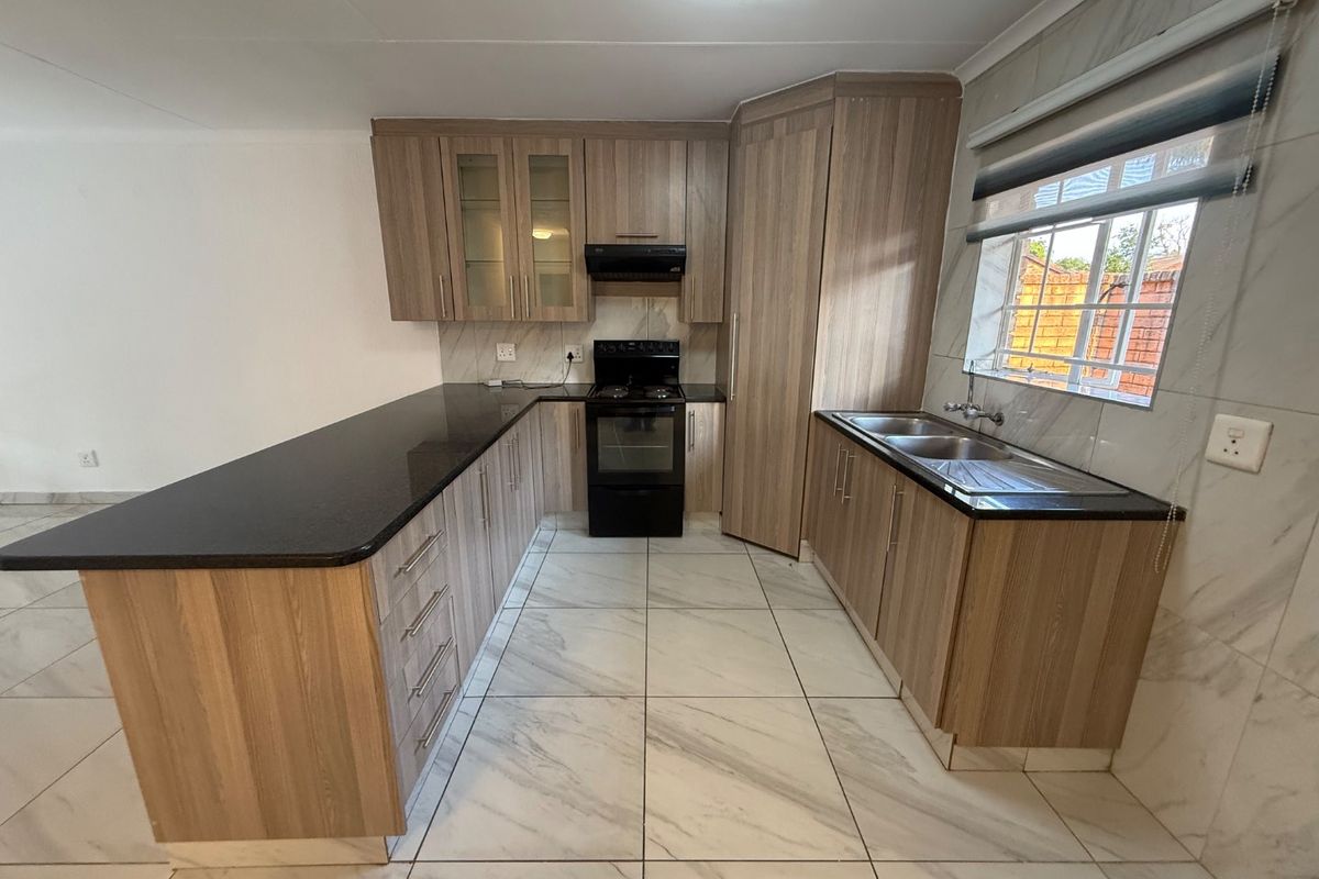 Modern kitchen featuring wood-finish cabinetry, granite countertops, a double sink, and a freestanding stove with an extractor fan.