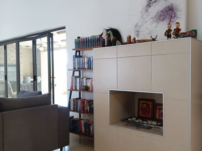 A bright living room featuring a modern tiled fireplace, vaulted ceilings, and large bi-fold glass doors leading to an outdoor patio area.