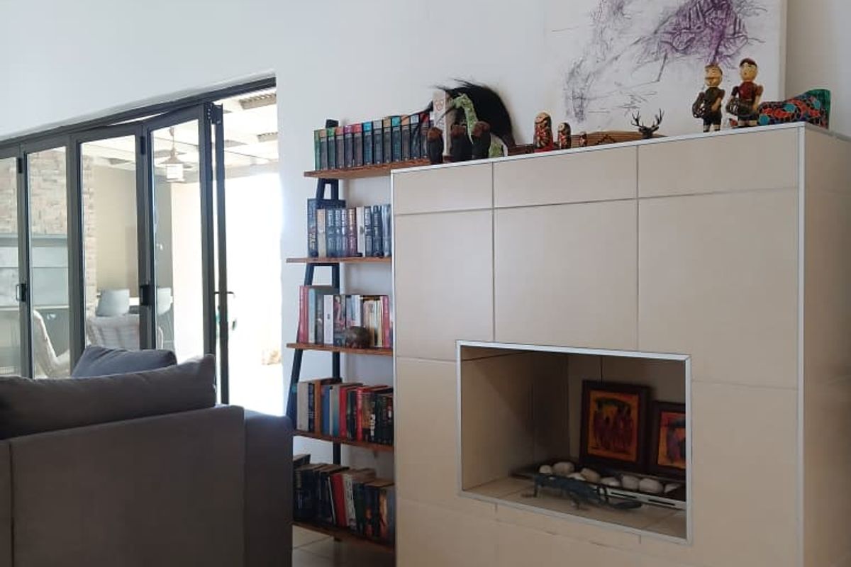 A bright living room featuring a modern tiled fireplace, vaulted ceilings, and large bi-fold glass doors leading to an outdoor patio area.
