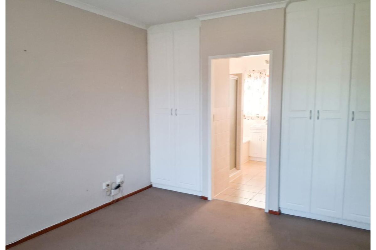 A bedroom featuring built-in wardrobes and an en-suite bathroom, finished with neutral wall tones and carpeted flooring.