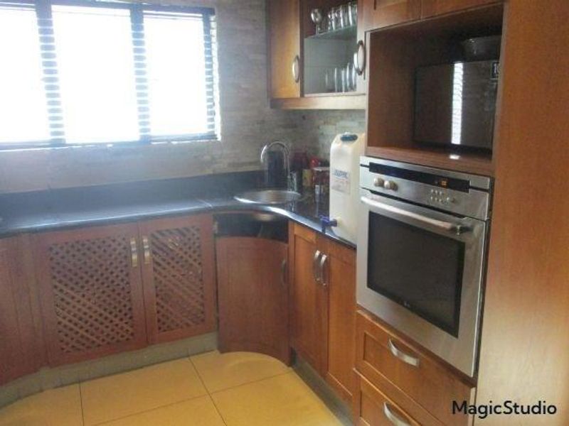 A functional kitchen featuring wooden cabinetry, built-in oven and microwave, stone tile backsplash, and a stainless steel sink with a window view.