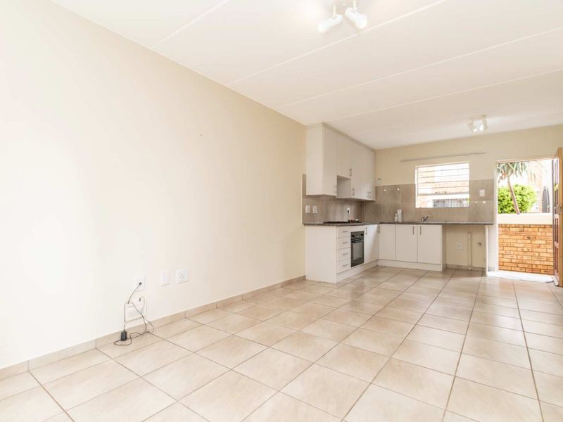 An open-plan living and kitchen area featuring neutral tiled flooring, built-in cabinetry, and direct access to an outdoor space.