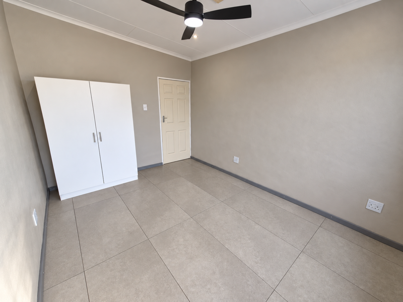 A clean, neutral bedroom featuring large format floor tiles, a modern ceiling fan, and a built-in wardrobe.