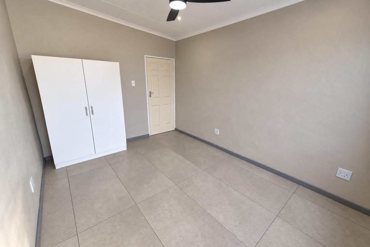 A clean, neutral bedroom featuring large format floor tiles, a modern ceiling fan, and a built-in wardrobe.