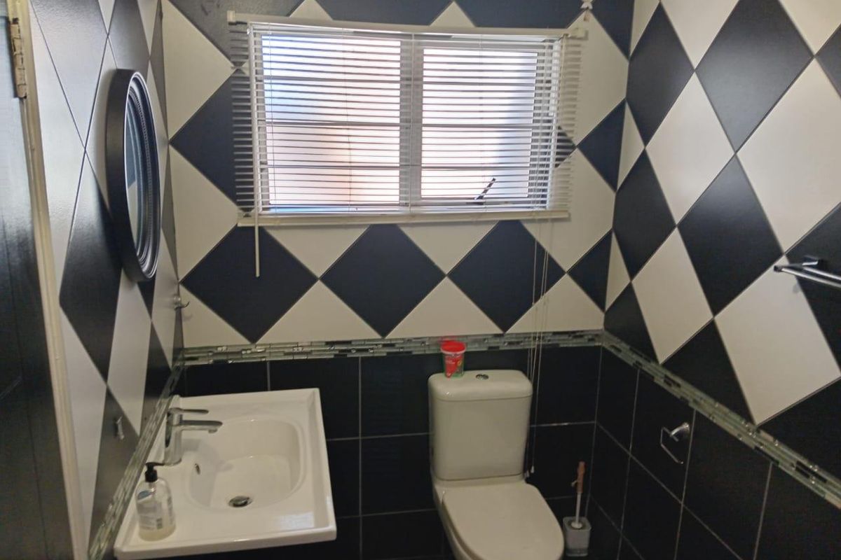 A compact bathroom featuring a wall-mounted basin, toilet, and distinctive black and white diamond-patterned wall tiling.