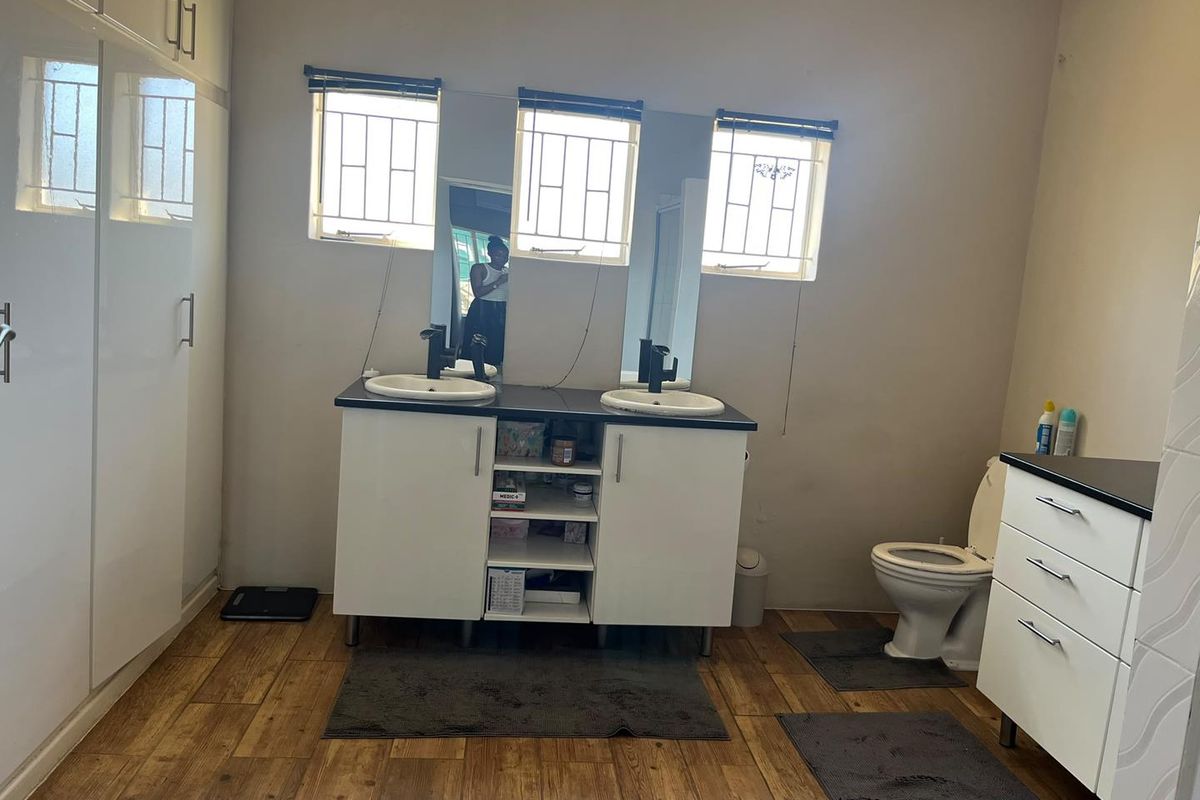 A functional bathroom featuring a double vanity with built-in cabinetry, a toilet, and wood-look tile flooring with security bars on the windows.