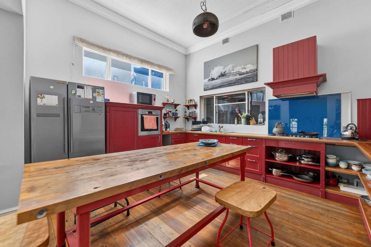 A spacious kitchen featuring red cabinetry, timber countertops, a central island, and high ceilings with a classic beadboard finish.