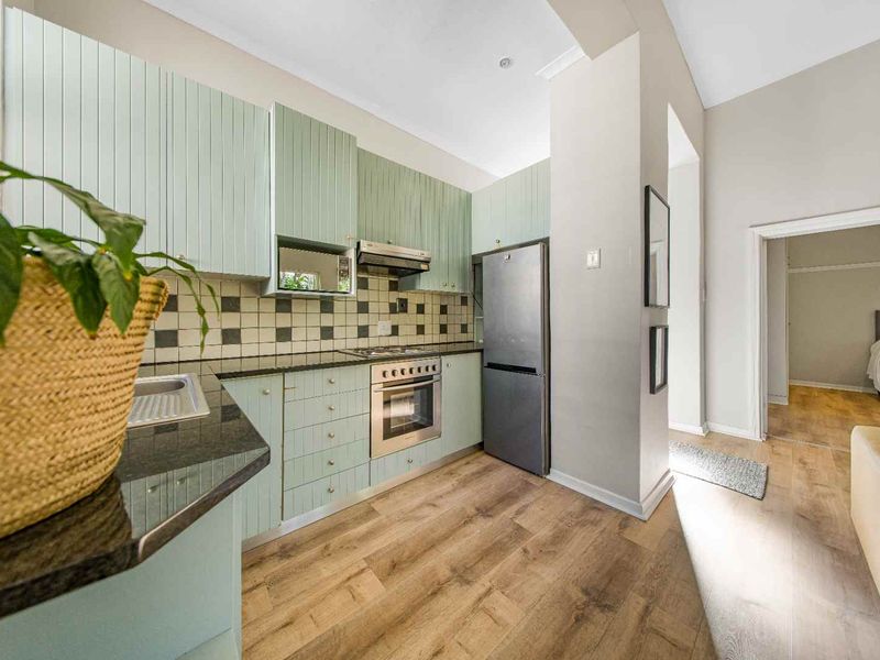 A functional kitchen featuring light green cabinetry, granite countertops, a tiled backsplash, and integrated appliances, with laminate flooring throughout.